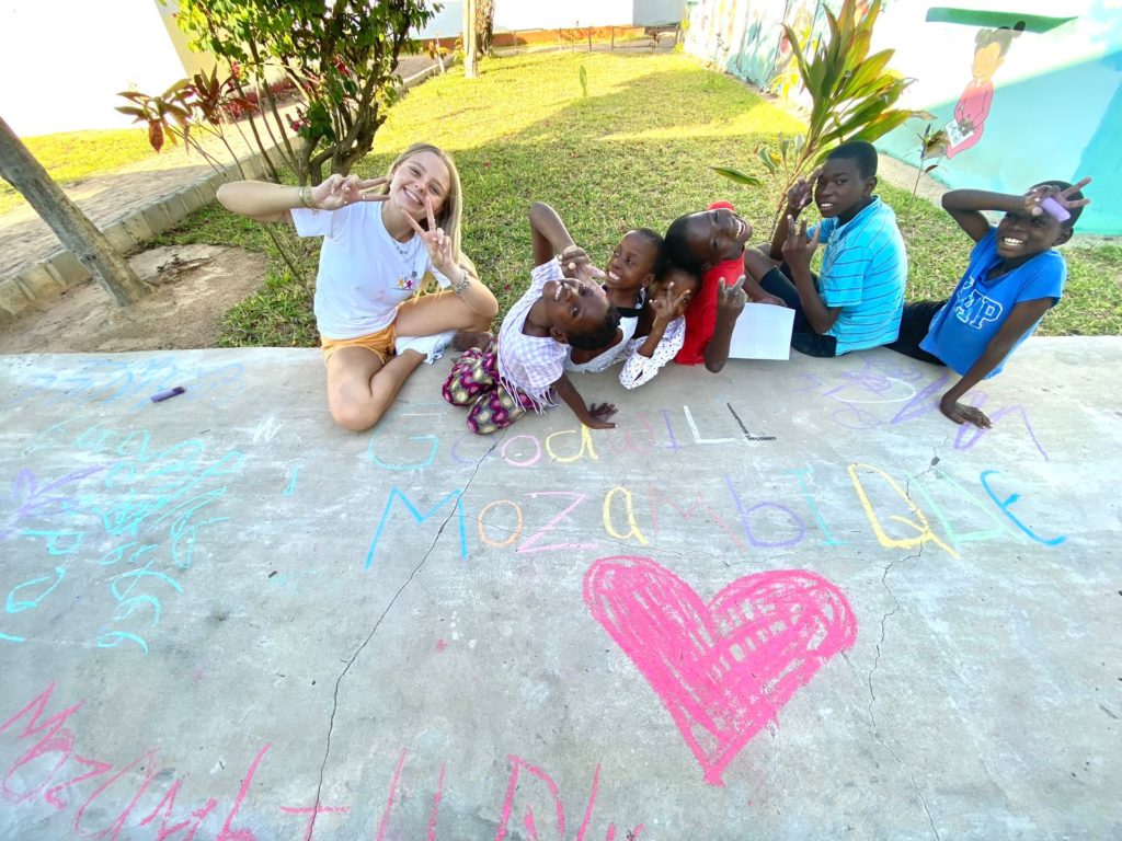Children and a volunteer beside Goodwill Mozambique drawn in chalk on the paving